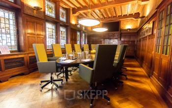 Elegant conference room with high-backed chairs around a long table, featuring wood-paneled walls and stained glass windows in Amsterdam Center.