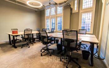 Bright office space with modern desks and mesh chairs, ideal for office space rental at Nieuwezijds Voorburgwal 104-108, Amsterdam Center. Large windows provide natural light, creating a pleasant work environment.