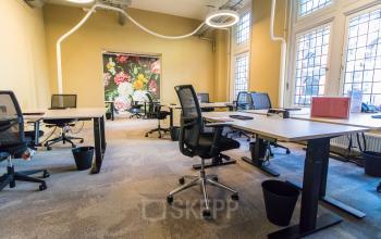 Bright office space with modern workstations and charming floral wall art, available for rent at Nieuwezijds Voorburgwal 104-108, Amsterdam Center. Perfect for dynamic and creative professionals seeking office space rental.