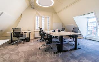 Bright office space for rent in Amsterdam Center, showcasing a furnished area with desks and chairs under a unique circular light fixture.
