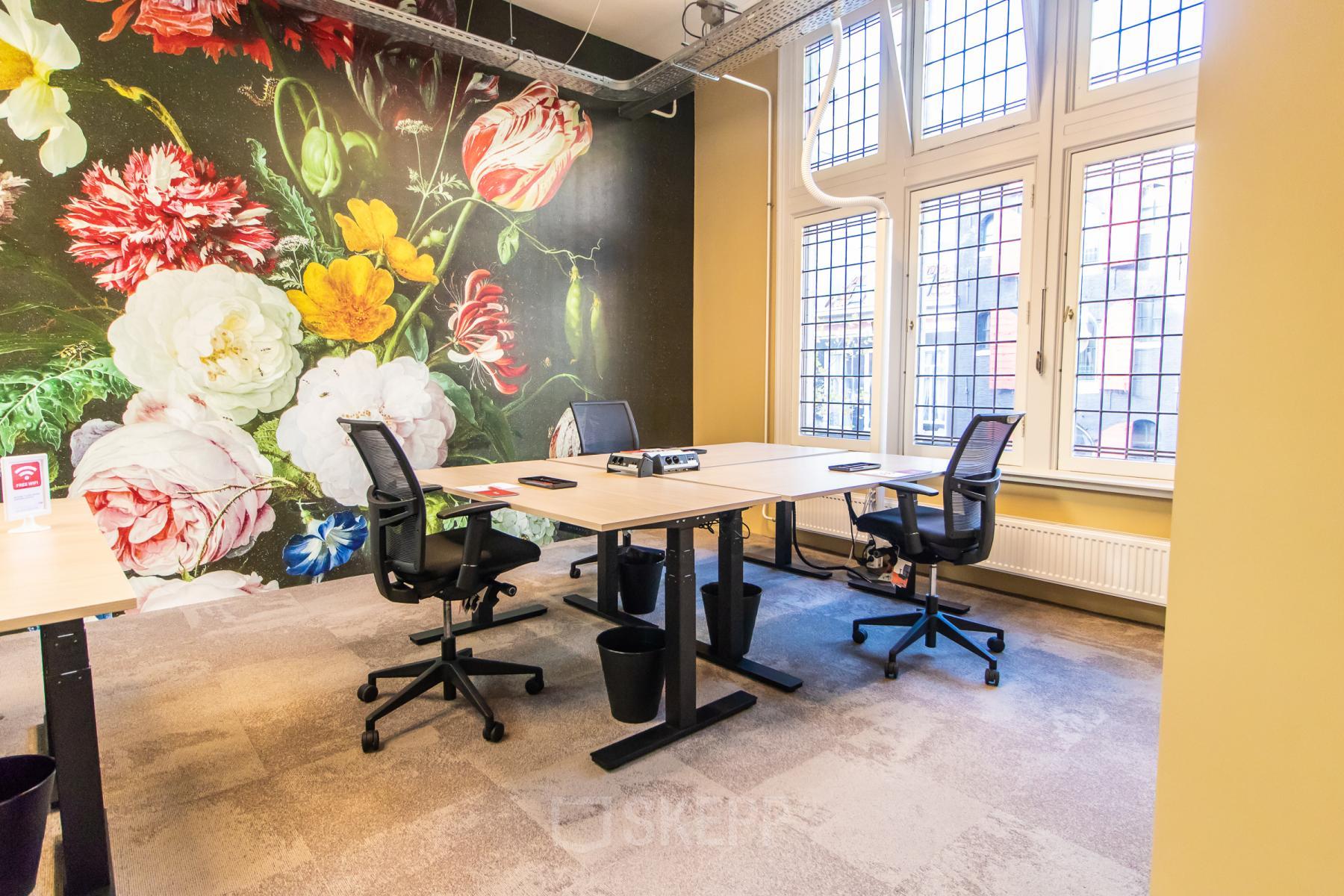 Bright office space for rent in Amsterdam Center, featuring modern furnishings and large windows. Ideal for business activities against a vibrant floral mural.