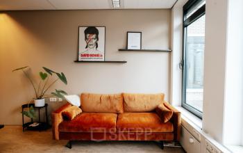Cozy office space rental in Amsterdam De Schinkel, featuring a stylish orange sofa and large windows. Ideal for those looking to rent office space at IJsbaanpad 2.