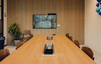 Modern conference room at IJsbaanpad 2, Amsterdam De Schinkel, ideal for office space rental, featuring a large table, chairs, a wall-mounted screen, and decor.