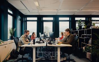 People engaged in business activities at IJsbaanpad 2, Amsterdam De Schinkel, in a furnished office space available for rent, featuring multiple workstations and abundant natural light.