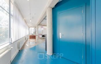 Bright office interior with large windows, blue floors, and blue doors located at Generaal Vetterstraat 77e, Amsterdam De Schinkel. Ideal office space rental for creative businesses.