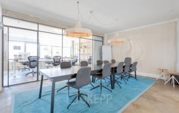 Modern office space with a large meeting table and chairs located at Generaal Vetterstraat 77e, Amsterdam De Schinkel. Bright workspace with glass walls and contemporary lighting.