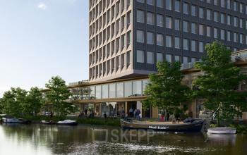 Exterior view of office building at Rijnsburgstraat 9-11 in Amsterdam De Schinkel, featuring modern architecture near a canal with boats and people walking outside.