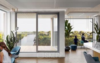 Modern workspace with wooden flooring, large windows, and minimalistic furnishings at Rijnsburgstraat 9-11, Amsterdam De Schinkel. Two people standing by the tall windows with a scenic view of green trees and water.