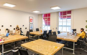 Bright office to rent at Herengracht 420, Amsterdam Canal Belt, featuring wooden desks, chairs, and people working on laptops.