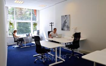 Office space rental at Herengracht 420 in Amsterdam Canal Belt, featuring multiple workspaces with desks, chairs, and natural light from large windows.