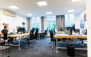 Modern furnished office space with multiple desks and chairs at Herengracht 420, in Amsterdam Canal Belt, Amsterdam. A person is working at a desk.