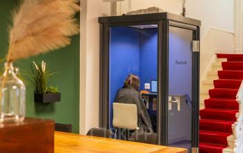 Interior view of office space rental at Herengracht 420, Amsterdam with a person working in a private booth, set against a backdrop of a green accent wall and red carpeted stairs.