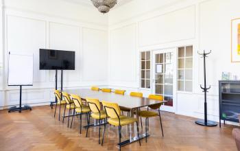 Spacious conference room with large table, yellow chairs, TV screen, and flipchart in office space rental at Herengracht 420, Amsterdam Canal Belt.