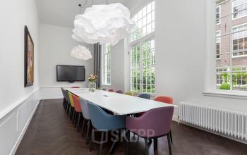 Bright conference room with a long white table and colorful chairs at Keizersgracht 62 – 64 in the Amsterdam Canal Belt, ideal for office space rental.