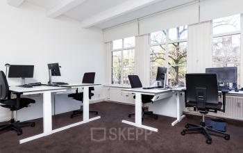 Bright office space with large windows, featuring several desks and chairs, ideal for office space rental in Amsterdam Canal Belt.