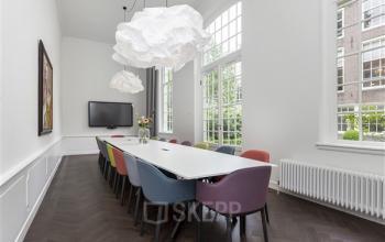 Bright, modern office space rental in Amsterdam Canal Belt, featuring a long table with colorful chairs under unique pendant lights, perfect for meetings.