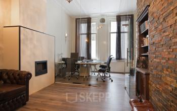 Elegantly furnished office space rental at Herengracht 282, featuring a classic brick wall, wooden floors, and stylish furniture in Amsterdam Canal Belt.