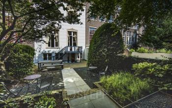 Serene office space rental in the garden of Herengracht 282 with lush greenery and outdoor seating, located in Amsterdam Canal Belt.