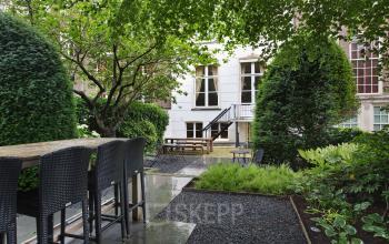 A serene garden patio at Herengracht 282 office space rental, Amsterdam Canal Belt, surrounded by lush greenery and outdoor seating.