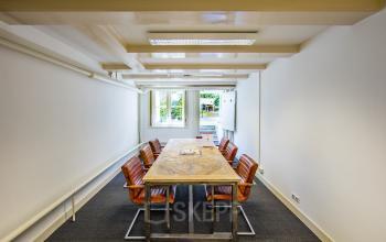 Chic office space rental at Herengracht 282, Amsterdam Canal Belt, with a large wooden table and comfortable seating.