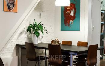 Office space rental at Vinkenstraat 79 HS, Amsterdam Canal Belt, featuring a modern meeting area with colorful artwork, wooden chairs, and a central table under stylish lighting.