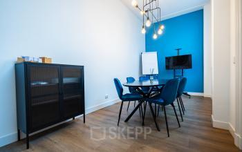 Office space rental at Keizersgracht 452 featuring a bright, modern conference room with blue accents and contemporary lighting. Features a TV, flip chart, and sleek furniture.