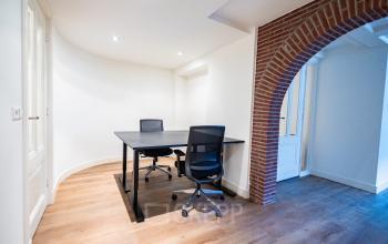 Office space rental at Keizersgracht 452, Amsterdam Canal Belt features a bright, minimalist workspace with wooden flooring and a brick archway, offering two desks with chairs for a productive environment.