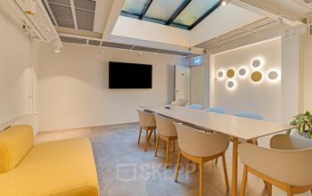 Modern conference room with a long wooden table, stylish chairs, and a smart wall display, located in the Amsterdam Canal Belt. Ideal for office space rental with its sleek, contemporary design.