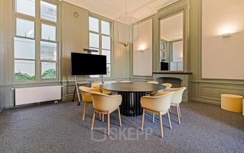 Stylish workspace at Keizersgracht 572-572, Amsterdam, featuring a large table, modern chairs, and a wall-mounted TV ideal for meetings. Prime office space rental in the Amsterdam Canal Belt.