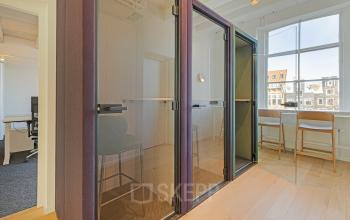 Modern workspace in Amsterdam Canal Belt featuring private booths with glass doors, hardwood floors, and natural light. Perfect for office space rental seeking privacy and style.