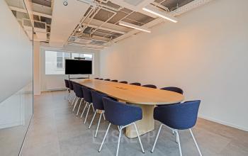 Modern conference room at Keizersgracht 572 in Amsterdam featuring a long wooden table, blue upholstered chairs, and a wall-mounted screen, ideal for meetings. Prime office space rental opportunity in the Canal Belt.