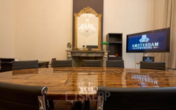 Elegant office space rental at Keizersgracht 391A featuring a polished wooden conference table, chic black chairs, and a vintage fireplace with a gold-framed mirror, perfect for professional meetings in Amsterdam Canal Belt.