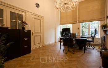 Interior view of a stylish office space rental at Keizersgracht 391A, Amsterdam Canal Belt, featuring elegant wooden floors, a chandelier, and modern office furniture ideal for business activities.