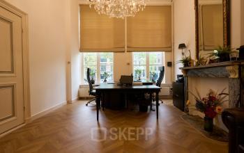 Charming office space rental at Keizersgracht 391A, Amsterdam, offering a bright interior with hardwood floors, elegant chandelier, and large windows overlooking the canal, perfect for productivity and style.