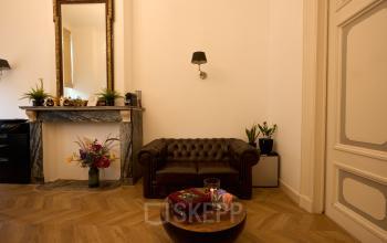 Charming office space rental at Keizersgracht 391A, Amsterdam Canal Belt. The interior features elegant wooden floors, a vintage sofa, and a decorative fireplace, creating a warm and inviting workspace.