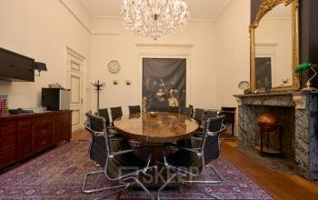 Elegant conference room at Keizersgracht 391A in Amsterdam, featuring a round wooden table with modern black chairs, an ornate fireplace, and a vintage globe, perfect for office space rental.