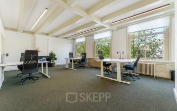 Bright office space with modern desks and chairs, large windows overlooking trees in the Amsterdam Canal Belt.