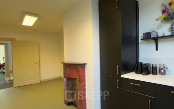 Interior view of an office space at Keizersgracht 261, Amsterdam Canal Belt, featuring a modern kitchenette with dark cabinets, countertop appliances, and a unique red-tiled fireplace surround.