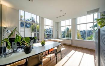 Bright office space rental in Amsterdam Canal Belt at Herengracht 582-584 with large windows, plants, and modern furniture.
