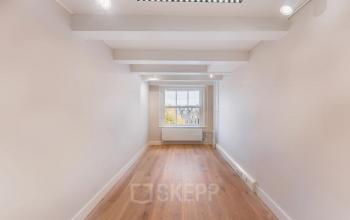 Unfurnished office space available for rent at Herengracht 582-584, Amsterdam Canal Belt, featuring wooden floors and large window with canal views.