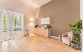 Bright and modern furnished office space with wooden flooring and natural light at Herengracht 582-584 in Amsterdam Canal Belt, available for rent. Features a cozy seating area and kitchenette.