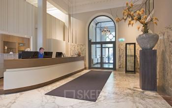 Elegant reception area in an office to rent at Herengracht 448-458 in Amsterdam Canal Belt, featuring a modern desk and marble flooring with a large vase decoration.