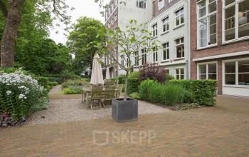 Exterior view of Herengracht 448-458, Amsterdam Canal Belt, showing a garden area with wooden tables and chairs surrounded by greenery.