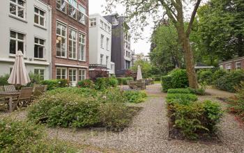 Exterior view of Herengracht 448-458, Amsterdam Canal Belt, featuring a serene garden with patio seating and greenery, ideal for office space rental.