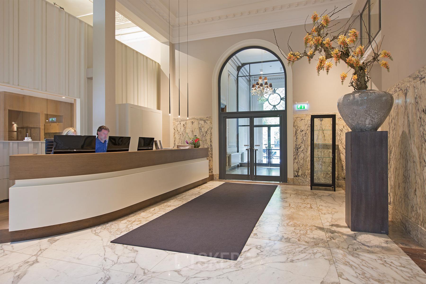 Elegant reception area in an office to rent at Herengracht 448-458 in Amsterdam Canal Belt, featuring a modern desk and marble flooring with a large vase decoration.