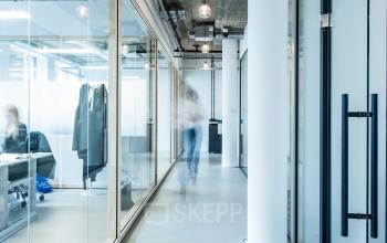 Modern office space rental at Singel 542, Amsterdam Canal Belt. Glass partitions and visible ceiling add a contemporary touch. Individuals are engaged in business activities.