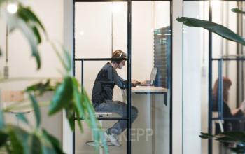 Two people working in a modern, glass-enclosed office space for rent on Singel 542, Amsterdam Canal Belt.