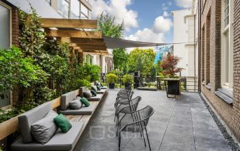 Outdoor seating area at Herengracht 459-469, ideal for office space rental with a mix of comfortable benches and modern chairs amid lush greenery.