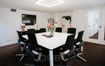 Modern, furnished conference room at Keizersgracht 97-99, Amsterdam Canal Belt, with a central square table, black chairs, flowers, and wall art.