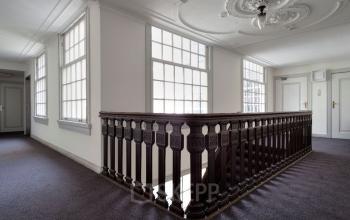 Interior view of Herengracht 495 office space rental in Amsterdam Canal Belt, featuring large windows, an ornate ceiling, and a classic wooden balustrade.
